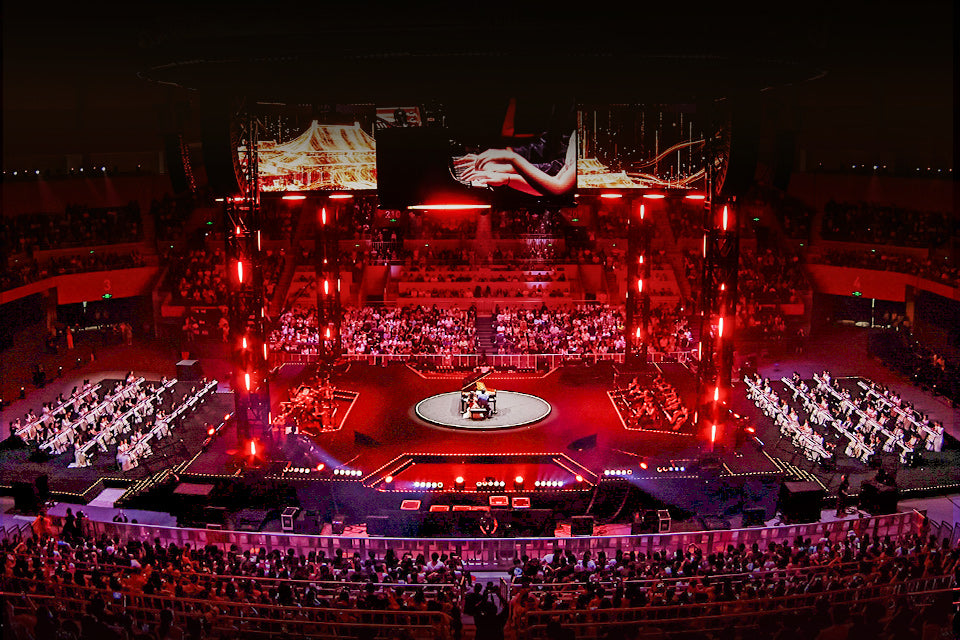 A red-lit concert arena with a central piano stage and young pianists performing on both sides