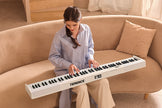 white digital piano being played by woman sitting on sofa in spacious living room